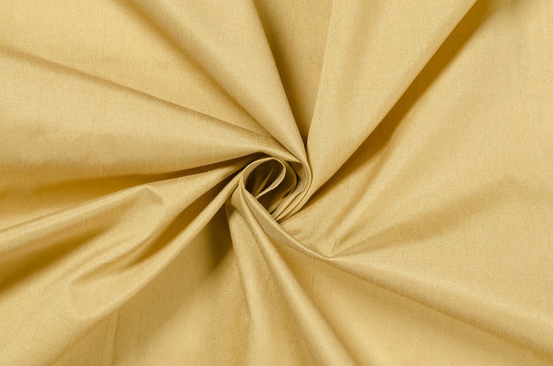 Puede incluir: Primer plano de una tela lisa de color amarillo dorado con un brillo sutil. La tela est&aacute; doblada y retorcida, creando un patr&oacute;n de remolino.