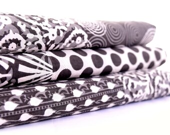 May include: A stack of three black and white patterned fabric squares. The top square has a swirling pattern, the middle square has a polka dot pattern, and the bottom square has a geometric pattern.