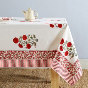 May include: White tablecloth with a red floral print. The tablecloth has a red and white striped border. A small white teapot sits on the tablecloth.