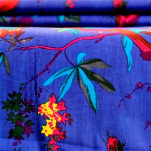 May include: Blue fabric with a colorful floral print featuring stylized leaves, flowers, and branches. The fabric has a textured surface.