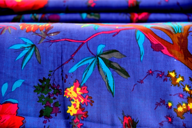 May include: Blue fabric with a colorful floral print featuring stylized leaves, flowers, and branches. The fabric has a textured surface.