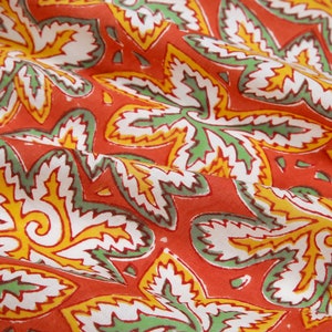 Pode incluir: Tecido vermelho com um padr&atilde;o floral branco, verde e amarelo. O tecido tem uma superf&iacute;cie texturizada e est&aacute; dobrado no centro.