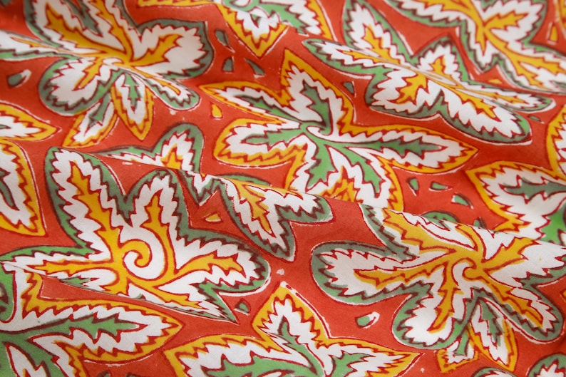 Pode incluir: Tecido vermelho com um padr&atilde;o floral branco, verde e amarelo. O tecido tem uma superf&iacute;cie texturizada e est&aacute; dobrado no centro.
