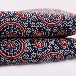 Op de afbeelding: Blauwe stof met een wit en rood paisley-patroon. De stof is dubbelgevouwen.