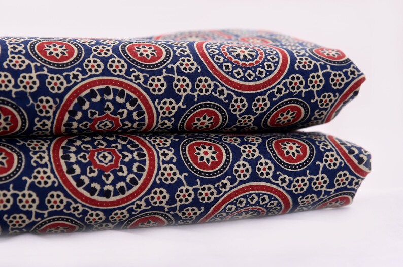 Op de afbeelding: Blauwe stof met een wit en rood paisley-patroon. De stof is dubbelgevouwen.