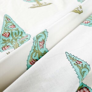 May include: White fabric with a repeating pattern of teal blue stylized trees with red flowers. The fabric is folded in half, showing the pattern on both sides.