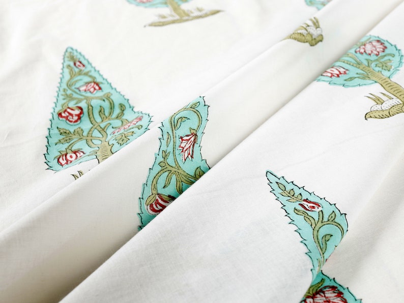 May include: White fabric with a repeating pattern of teal blue stylized trees with red flowers. The fabric is folded in half, showing the pattern on both sides.