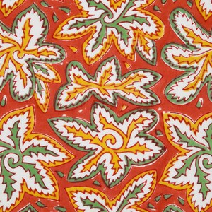Pode incluir: Um tecido vermelho com um padr&atilde;o repetitivo de folhas estilizadas verdes, brancas e amarelas. As folhas t&ecirc;m uma borda dentada e um desenho em espiral no centro.