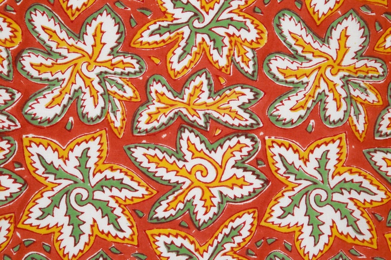 Pode incluir: Um tecido vermelho com um padr&atilde;o repetitivo de folhas estilizadas verdes, brancas e amarelas. As folhas t&ecirc;m uma borda dentada e um desenho em espiral no centro.