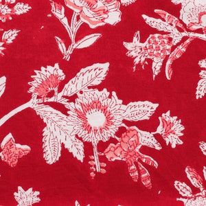 May include: Red fabric with a white floral pattern. The flowers are stylized and have pink accents. The fabric has a vintage look.