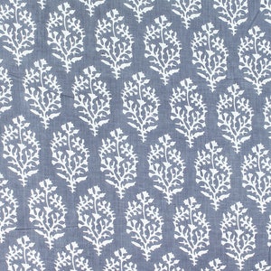 May include: Close-up of a fabric with a repeating pattern of white floral designs on a muted blue background. The floral elements resemble stylized branches or leaves, creating a textured, organic aesthetic. The fabric appears to be cotton or linen.
