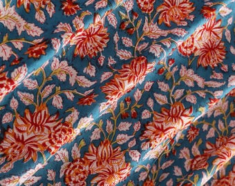 May include: Close-up of a teal fabric with a repeating floral pattern. The design features large orange and red flowers with white and green leaves and stems. The fabric is folded, creating shadows and depth.