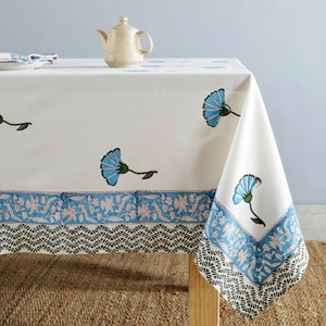 Pode incluir: Toalha de mesa de algod&atilde;o branco com estampa floral azul e borda preta e branca. A toalha de mesa tem uma borda festonada e &eacute; decorada com flores e folhas azuis.