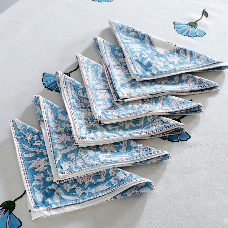 Pode incluir: Um conjunto de guardanapos de algod&atilde;o azul e branco com estampa floral. Os guardanapos s&atilde;o dobrados em forma triangular e t&ecirc;m uma borda branca.