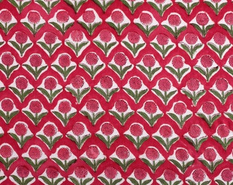 Può includere: Un tessuto rosso con un motivo floreale bianco e verde ripetuto. Il motivo floreale è un fiore stilizzato con un centro circolare e cinque petali.
