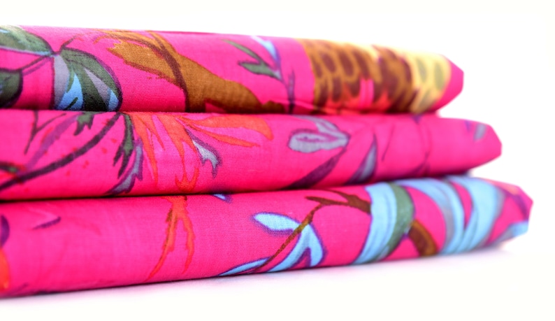 May include: A stack of three pink fabric squares with a colourful floral pattern. The fabric has a soft, flowing texture.
