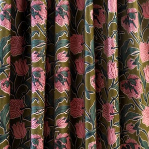 Pode incluir: Uma cortina de tecido com um padr&atilde;o floral repetitivo de tulipas cor-de-rosa com folhas e caules verde-escuros sobre um fundo verde-azeitona profundo. O material tem uma textura macia semelhante a veludo com pregas verticais que criam profundidade.