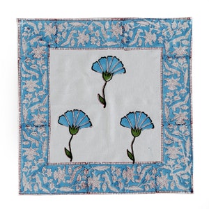 Pode incluir: Um guardanapo de algod&atilde;o branco com um padr&atilde;o floral azul. O guardanapo tem uma borda azul e branca com um design floral.