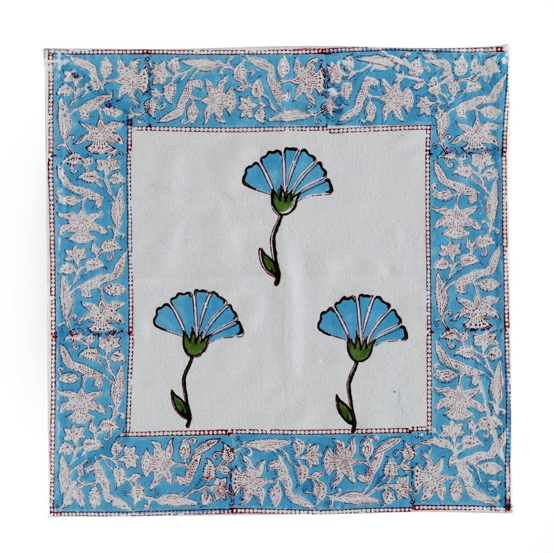 Pode incluir: Um guardanapo de algod&atilde;o branco com um padr&atilde;o floral azul. O guardanapo tem uma borda azul e branca com um design floral.