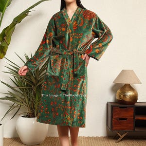 May include: A green velvet robe with a floral print. The robe has a shawl collar, long sleeves, and a tie belt.