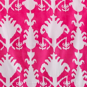 Op de afbeelding: Witte stof met een roze en wit ikat-patroon. Het patroon is een herhalend ontwerp van gestileerde bloemen.