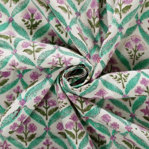 May include: White fabric with a repeating pattern of green and purple flowers. The fabric is folded and twisted.