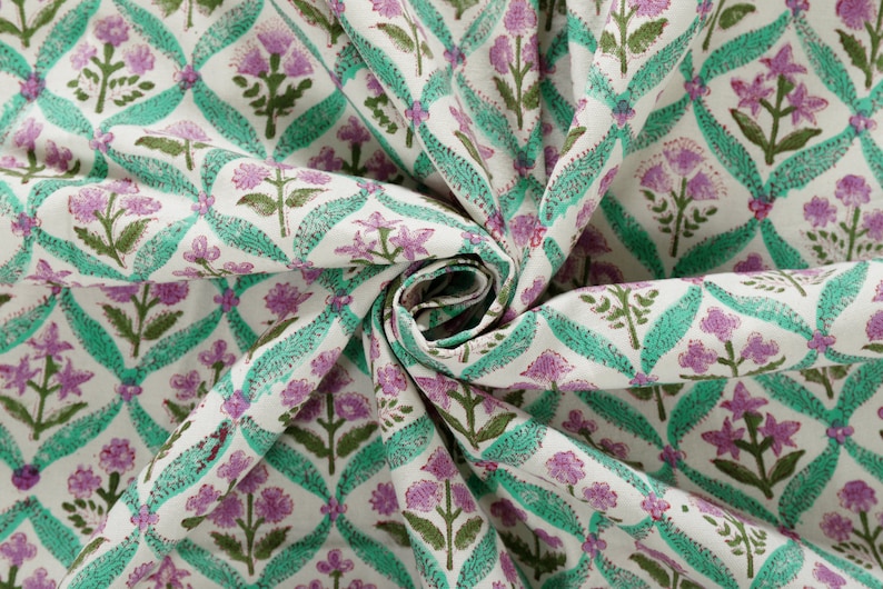 May include: White fabric with a repeating pattern of green and purple flowers. The fabric is folded and twisted.