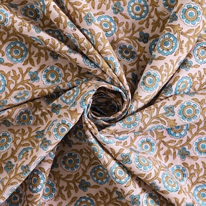 May include: A close-up of a beige fabric with a repeating pattern of blue and brown floral designs. The fabric is folded and twisted, creating a swirling effect.