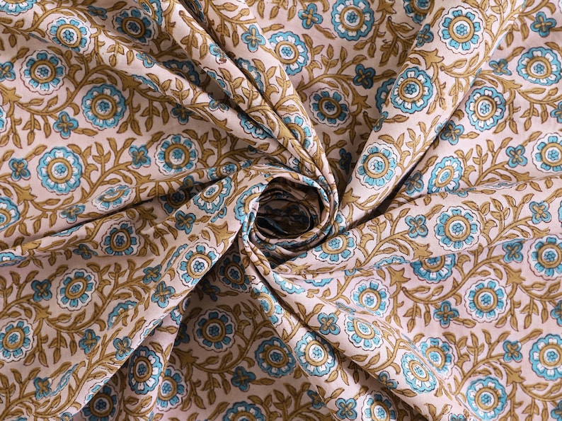 May include: A close-up of a beige fabric with a repeating pattern of blue and brown floral designs. The fabric is folded and twisted, creating a swirling effect.
