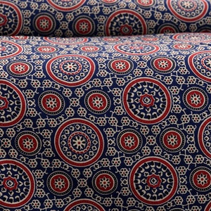 Op de afbeelding: Een blauwe stof met een herhalend patroon van rode, witte en zwarte cirkels. De cirkels hebben ingewikkelde ontwerpen in hun binnenste.
