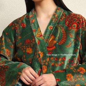 May include: A green velvet robe with a floral print in shades of orange, red, and yellow. The robe has a shawl collar and a tie belt.