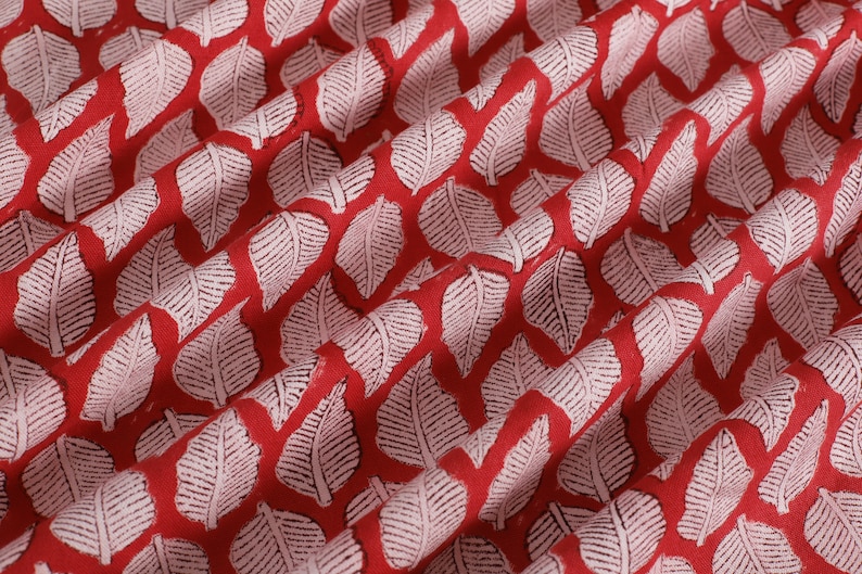 May include: Red fabric with a white leaf pattern. The leaves are a repeating pattern and are slightly raised.