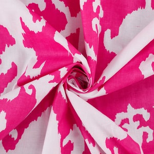 Op de afbeelding: Witte stof met een roze abstracte print. De stof is gevouwen en gedraaid, waardoor het patroon zichtbaar wordt.