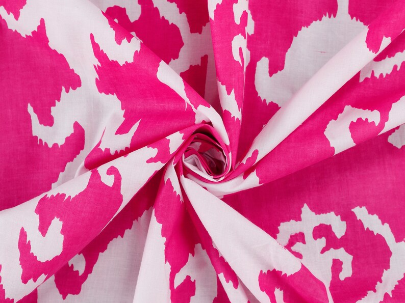 Op de afbeelding: Witte stof met een roze abstracte print. De stof is gevouwen en gedraaid, waardoor het patroon zichtbaar wordt.