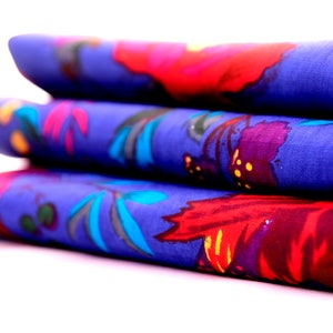 May include: A stack of three blue fabric napkins with a floral pattern in shades of red, purple, and blue.