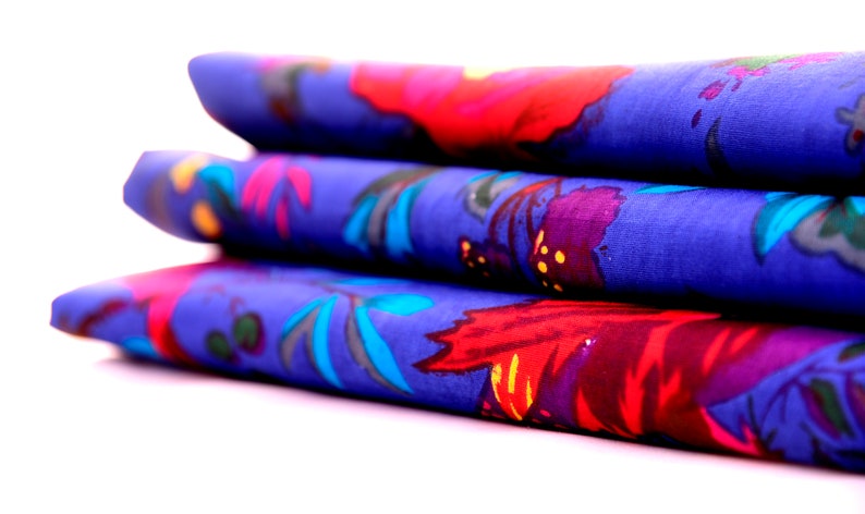 May include: A stack of three blue fabric napkins with a floral pattern in shades of red, purple, and blue.