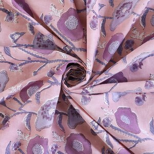 May include: Pink fabric with a floral print in shades of purple. The fabric is folded and shows the pattern repeating.