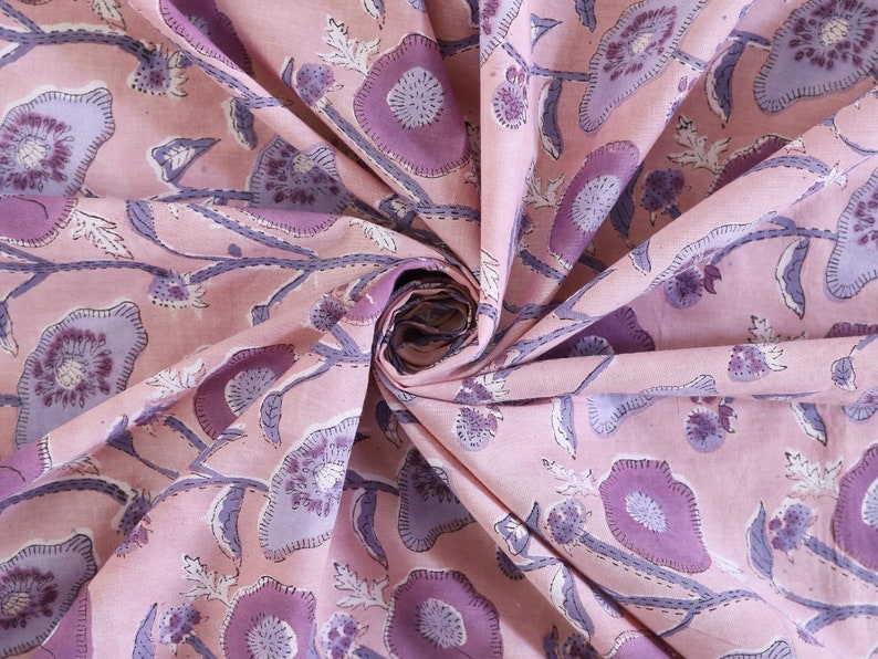 May include: Pink fabric with a floral print in shades of purple. The fabric is folded and shows the pattern repeating.
