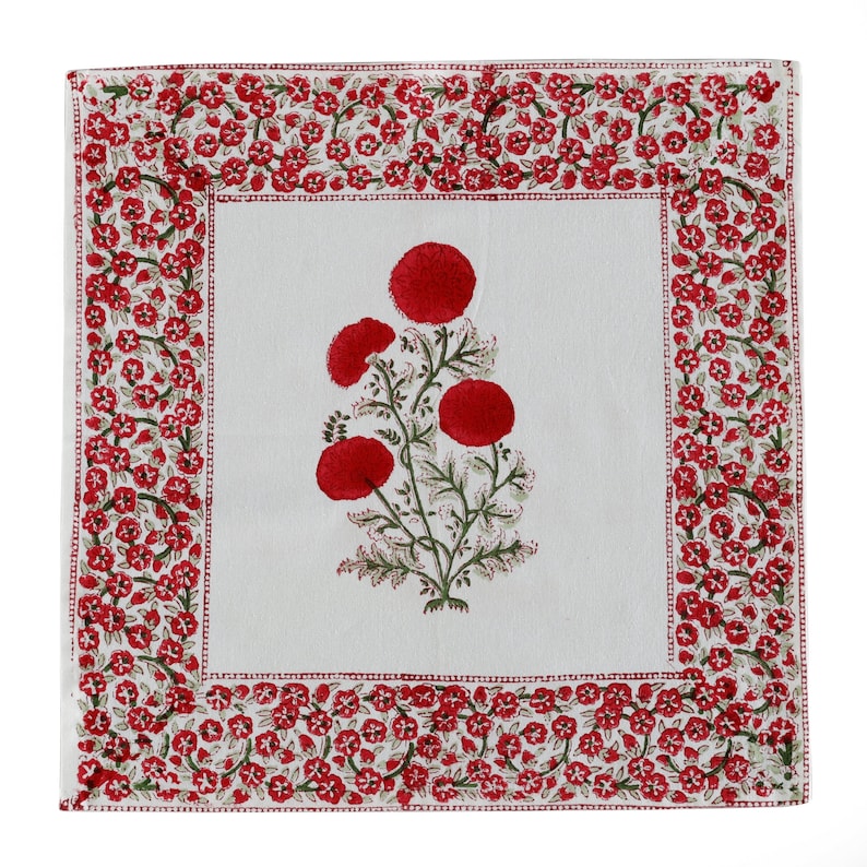 May include: White cotton square table runner with a red floral design. The floral design features a cluster of red flowers with green leaves and stems. The border of the runner is a repeating pattern of small red flowers.