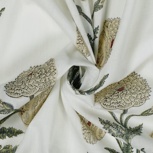 Op de afbeelding: Witte katoenen stof met een bloemenprint. De stof heeft een herhalend patroon van grote, gestileerde bloemen met groene bladeren. De bloemen zijn lichtbeige van kleur met donkerbruine contouren.