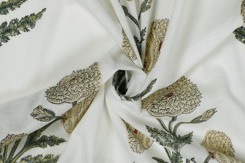 Op de afbeelding: Witte katoenen stof met een bloemenprint. De stof heeft een herhalend patroon van grote, gestileerde bloemen met groene bladeren. De bloemen zijn lichtbeige van kleur met donkerbruine contouren.
