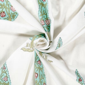 May include: White fabric with a repeating pattern of green and blue stylized floral designs. The fabric is folded and twisted, showing the pattern from different angles.