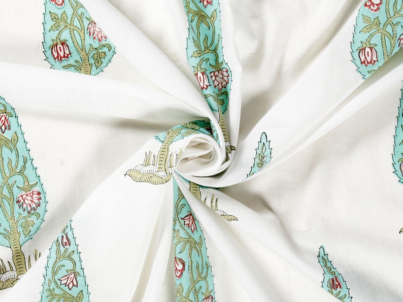 May include: White fabric with a repeating pattern of green and blue stylized floral designs. The fabric is folded and twisted, showing the pattern from different angles.