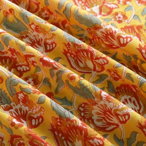 Puede incluir: Tela amarilla con un patr&oacute;n floral en tonos rojos, naranjas y verdes. La tela est&aacute; doblada y tiene un tacto suave y texturizado.