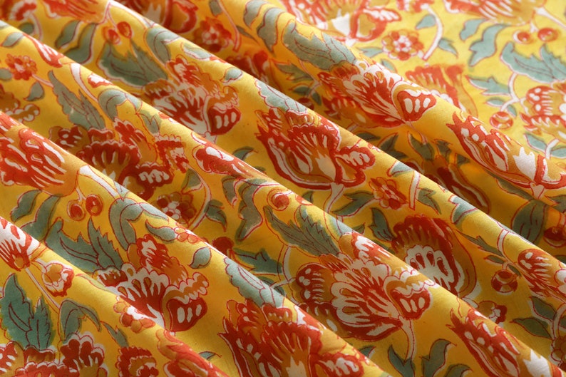 Puede incluir: Tela amarilla con un patr&oacute;n floral en tonos rojos, naranjas y verdes. La tela est&aacute; doblada y tiene un tacto suave y texturizado.