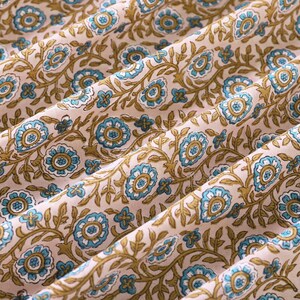 May include: A close-up of a fabric with a repeating pattern of blue and brown flowers on a light pink background.