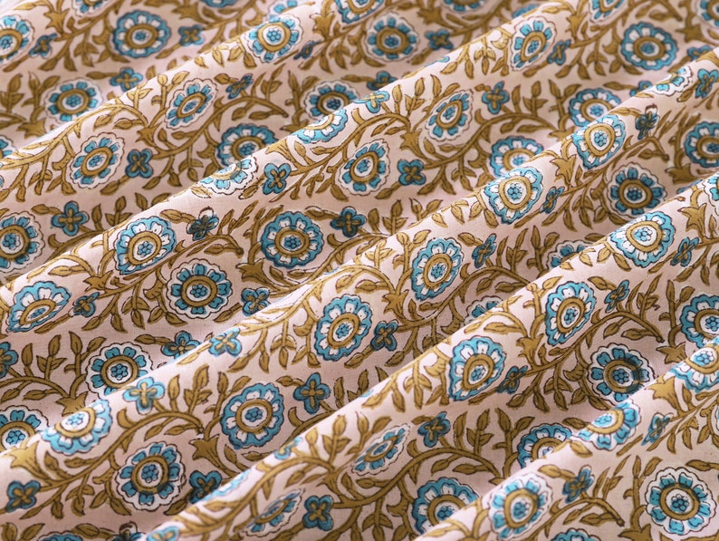 May include: A close-up of a fabric with a repeating pattern of blue and brown flowers on a light pink background.