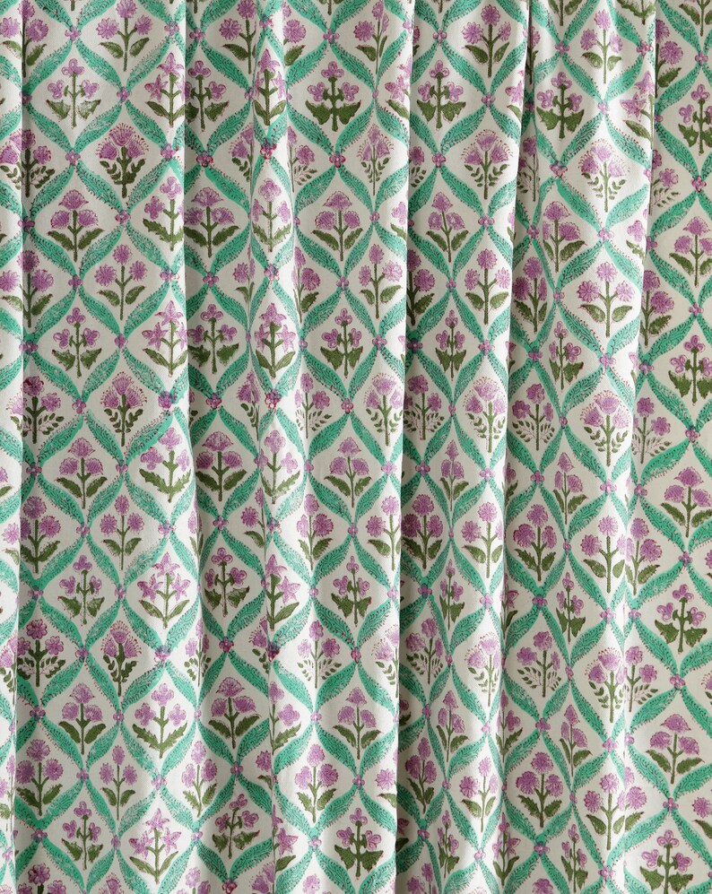 May include: White fabric with a repeating pattern of green and purple floral designs. The pattern features a diamond shape with a floral motif in the center.