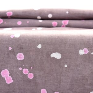 May include: A close-up of a folded piece of fabric with a gray background and pink and white splatter paint.