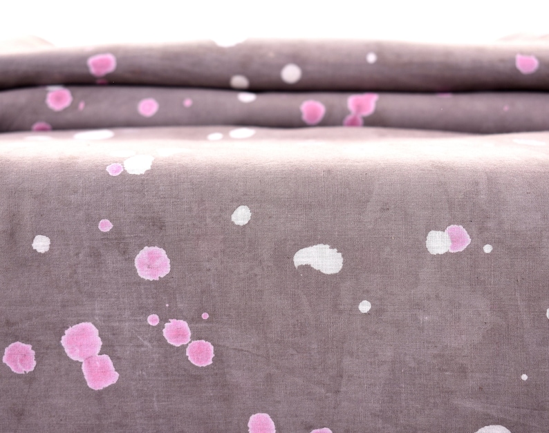 May include: A close-up of a folded piece of fabric with a gray background and pink and white splatter paint.